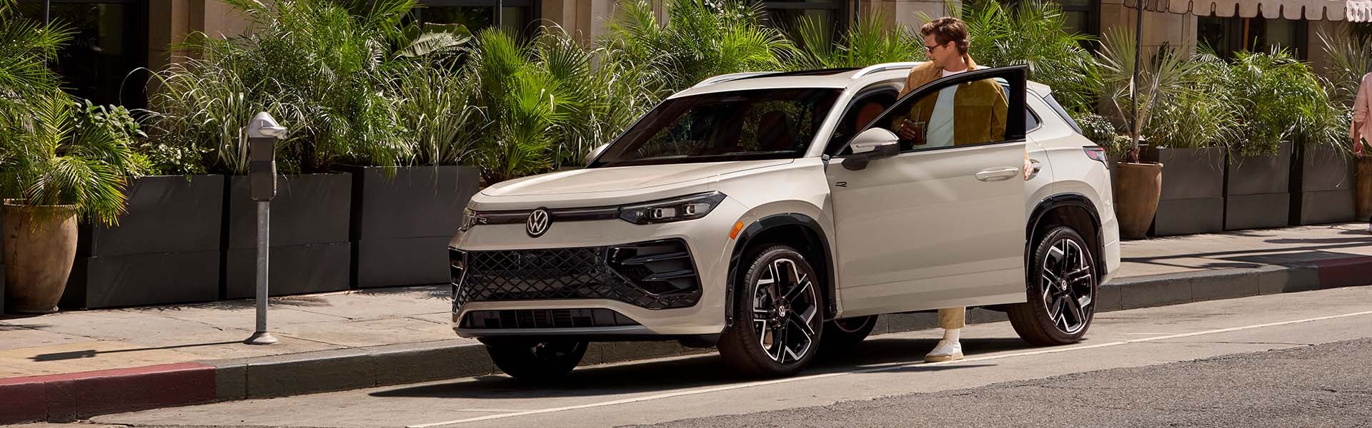 White Volkswagen SUV parked on city street with person opening driver door near greenery